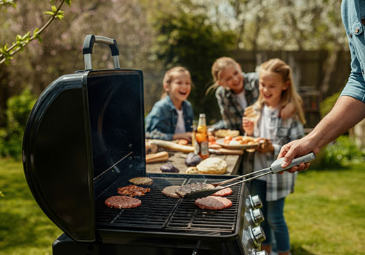 Family grilling burgers outdoors on a sunny day with food and drinks on a picnic table nearby