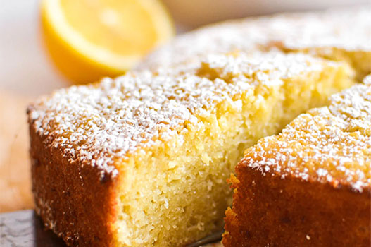 Round olive oil cake dusted with powdered sugar on a white cake stand with citrus slices