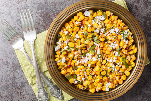 Grilled corn and sweet onion salad topped with crumbled cheese in a dark bowl with two forks